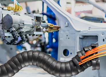 Chaîne porte-câbles triflex devant un robot d'assemblage de voitures